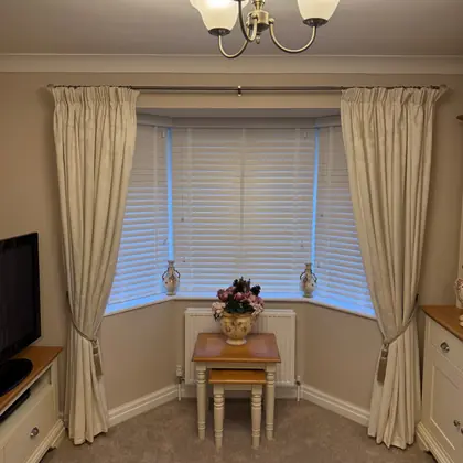 A venetian blind fitted inside a bay window, with the customer's curtains left in place